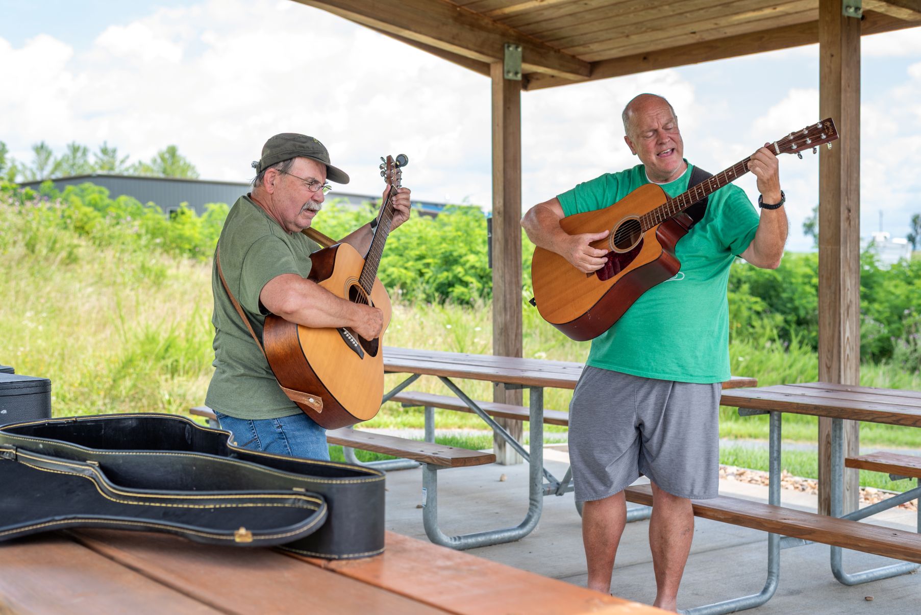Two men playing guitars in the outdoor shelter at The Trails at Mill Place Park.